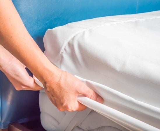 Woman is putting the bedding cover or mattress pad on the bed or putting off for cleaning process.