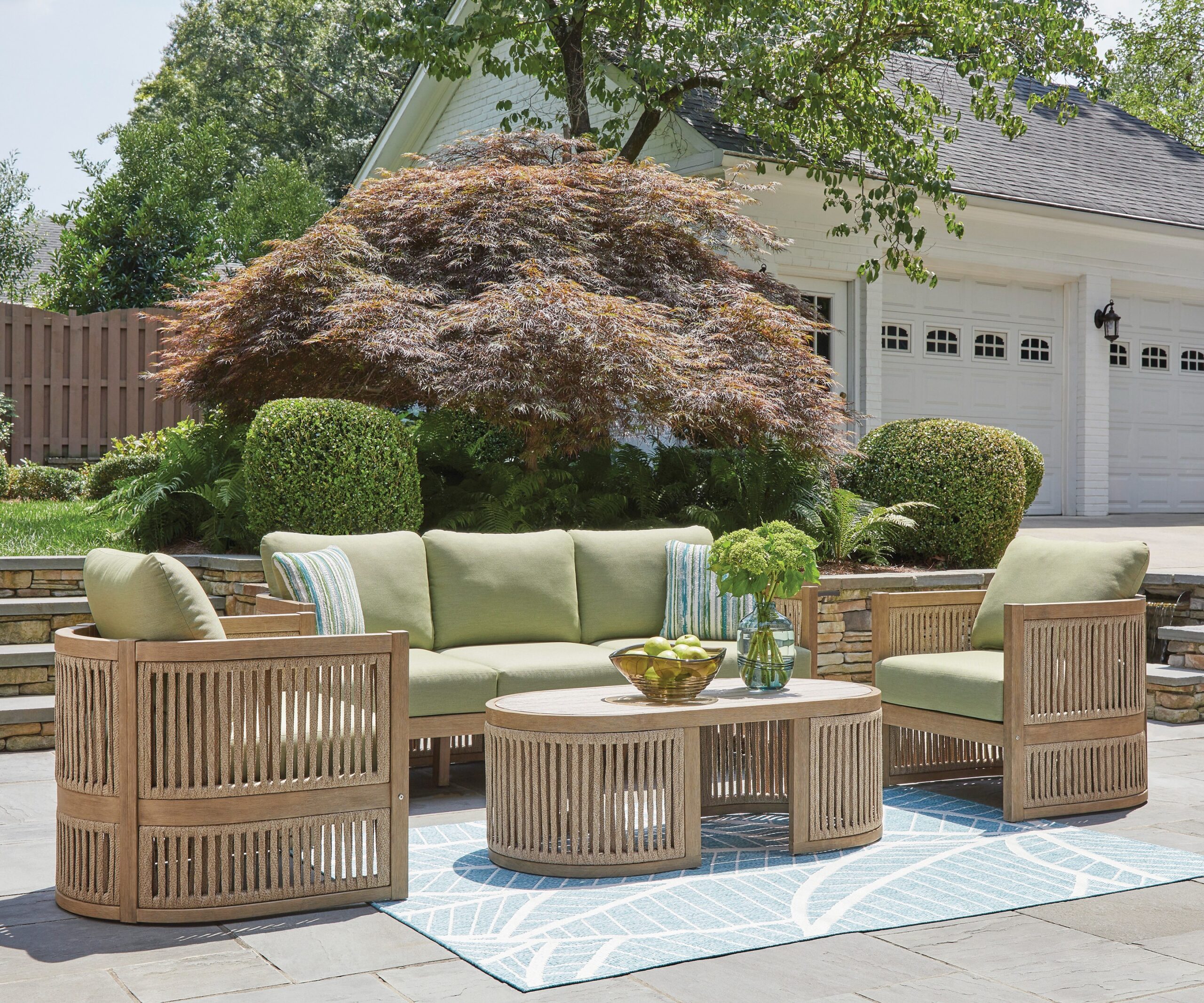 An outdoor lifestyle photo of a green and teak colored sofa, chairs and coffee table.